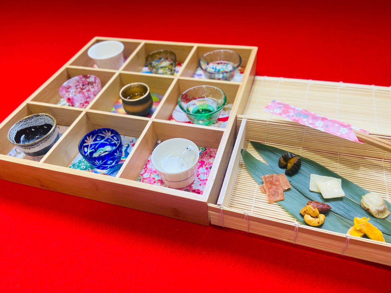 A nine-cup sake tray beside a bamboo tray of snacks